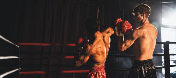 Aziatische en Kaukasische Muay Thaise bokser ontketent elleboogaanval in felle bokstraining, het leveren van elleboogslag aan sparringtrainer, showcasing bokstechniek en vaardigheid. Aansporing - Foto, afbeelding