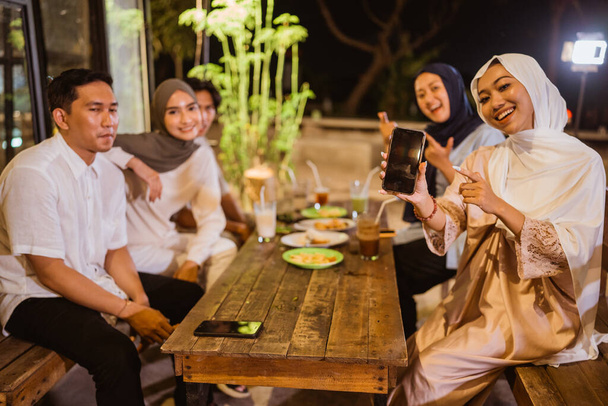 Muslim woman and friends show screen phone while breaking fast together at outdoor cafe - Fotoğraf, Görsel