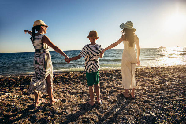 Мати та діти тримаються за руки, насолоджуючись заходом сонця на пляжі. Щасливі сімейні подорожі та відпочинок концепція. - Фото, зображення