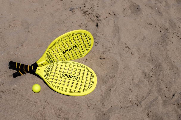 Beach tennis racket and ball of yellow color on tne beach.Copy space.Summer sport background. - Φωτογραφία, εικόνα