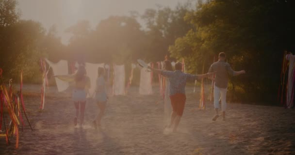 Αργή κίνηση πλάνο χαρούμενων νεαρών ανδρών και γυναικών που τρέχουν απολαμβάνοντας το ηλιοβασίλεμα στην παραλία - Πλάνα, βίντεο