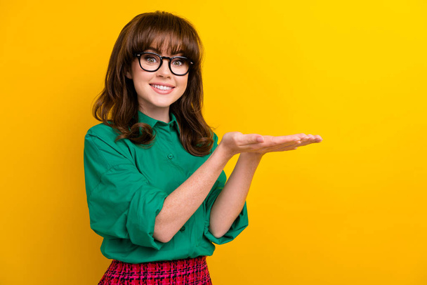 Photo of lovely nice person beaming smile hands palms hold empty space proposition isolated on yellow color background. - 写真・画像