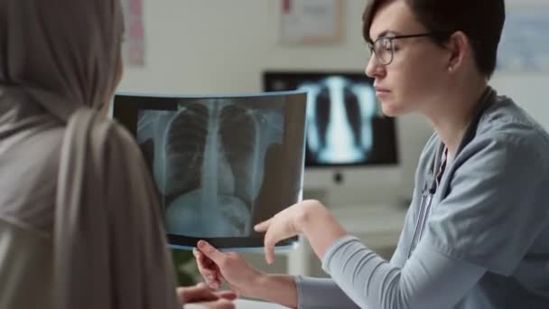 Röntgen detayları ve konsültasyonun tanımı ve sunumu sırasında önündeyken tesettürdeki hastaya tıbbi muayenenin sonucunu gösteren kendinden emin bir kadın radyoloji uzmanı. - Video, Çekim