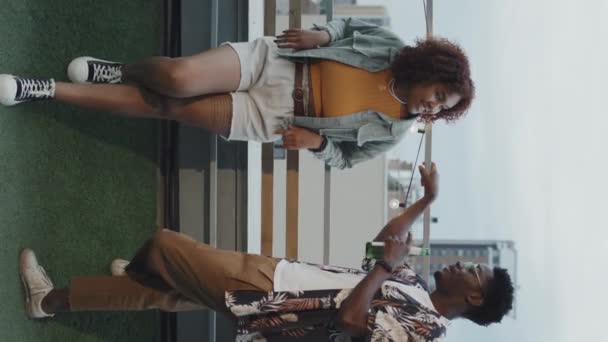 Vertical slow motion shot of young Black man and woman wearing stylish casual clothes relaxing on rooftop on summer evening - Footage, Video