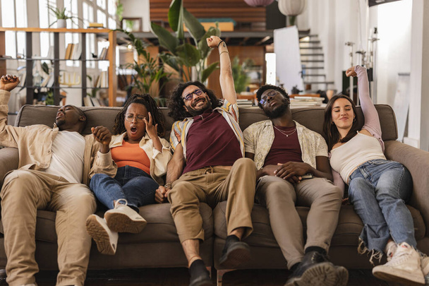 groep vermoeide multiraciale vrienden die gapen en hun armen uitstrekken zittend op de bank - Foto, afbeelding