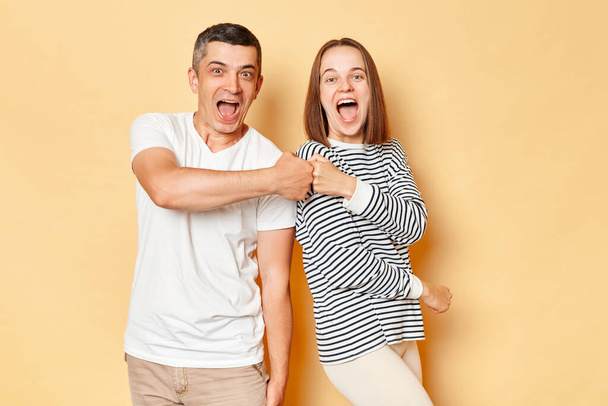 Excited laughing young couple friends man woman in casual clothing isolated over beige background making fist bump deal sreaming with happiness celebrating good idea. - Fotografie, Obrázek