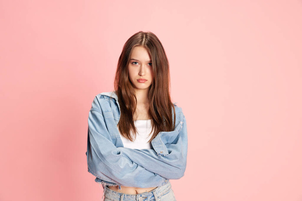 Portrait of young beautiful girl, student standing with serious face against pink studio background. Feeling offended. Concept of human emotions, fashion, youth, lifestyle, female beauty, ad - Photo, image