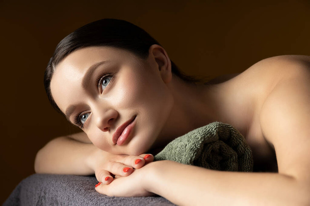 Молода брюнетка на масажі, коричневий фон - Фото, зображення