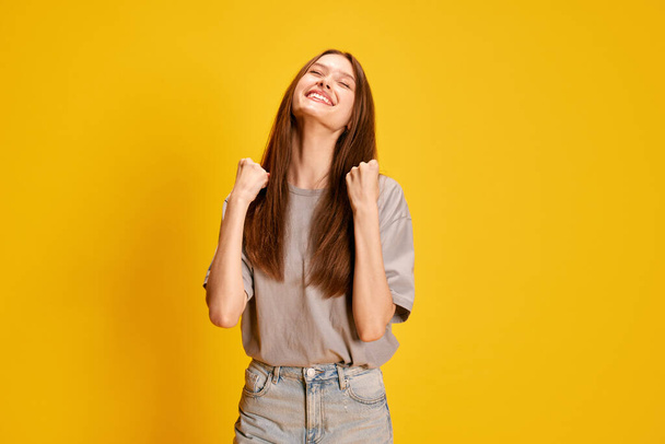 Portrait of young beautiful, emotive girl expressing happiness, success and win against yellow studio background. Concept of human emotions, fashion, youth, lifestyle, female beauty, ad - Фото, изображение