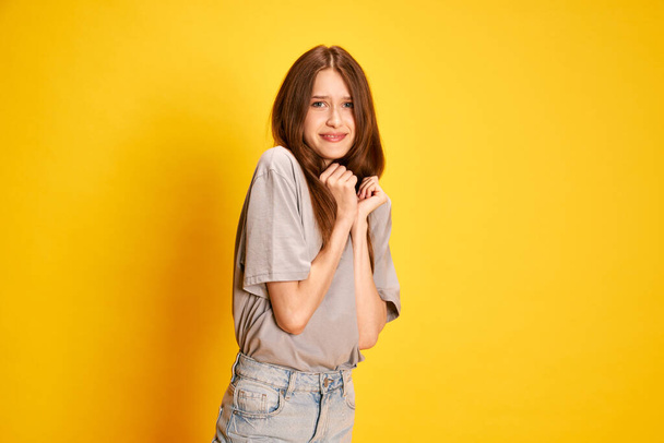Portrait of young beautiful girl emotionally posing with fearful, unpleasant face against yellow studio background. Concept of human emotions, fashion, youth, lifestyle, female beauty, ad - Fotografie, Obrázek