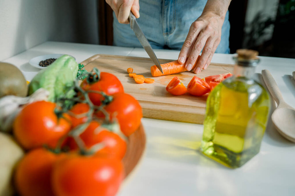 Zboża anonimowy gospodyni domowa cięcia marchewki w kuchni podczas przygotowywania zdrowej sałatki z pomidorami i ziołami podczas gotowania w domu - Zdjęcie, obraz