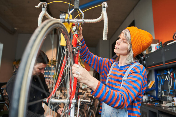 ワークショップで自転車を修理する女性の自転車整備士笑顔。現代のサイクル伝送システムを修正する若い女性。自転車のメンテナンスとスポーツショップのコンセプト - 写真・画像