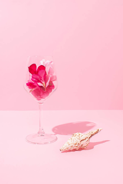 Üveg tele virágszirmok és kagyló fényes pasztell rózsaszín háttér. Nyári romantikus szertartás dekoráció. Ünneplés a tengerparton ötlet. - Fotó, kép