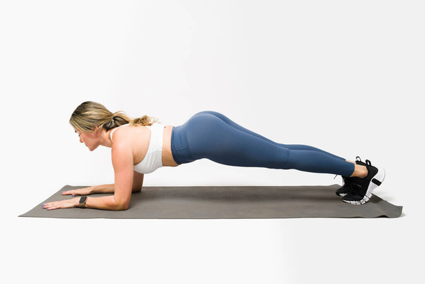 Seitenansicht einer starken, sportlichen Frau mit einer fitten Beute und einem Körper, der auf einer Trainingsmatte trainiert und eine Planke macht - Foto, Bild