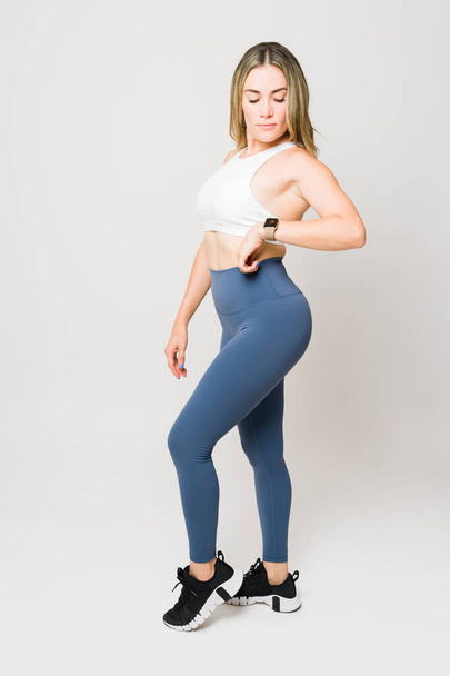 Volledige lengte van een sportieve atletische sterke vrouw poseren in activewear en met behulp van een smartwatch om haar workout run volgen - Foto, afbeelding