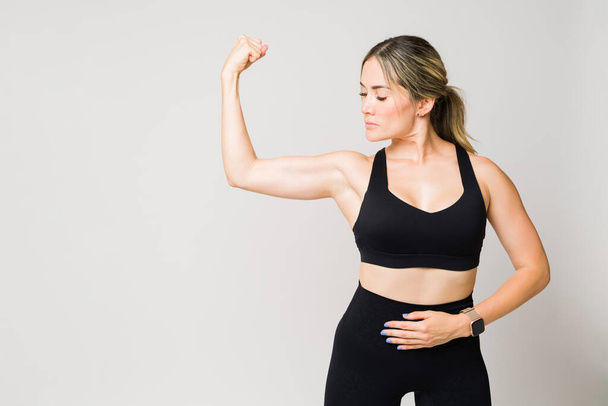 Ελκυστική καυκάσιος γυναίκα στα 30 της με πολλή δύναμη κάνει μια μπούκλα bicep και δείχνει τους μυς της μετά την άσκηση έξω - Φωτογραφία, εικόνα