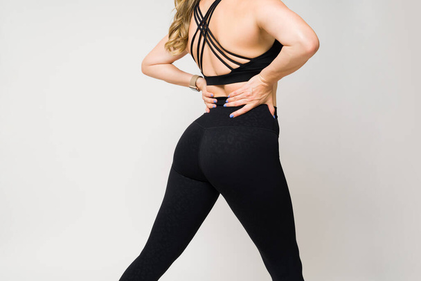 Close up de uma mulher caucasiana com um corpo apto em leggings pretos e activewear preto posando e mostrando seu estilo de vida fitness - Foto, Imagem
