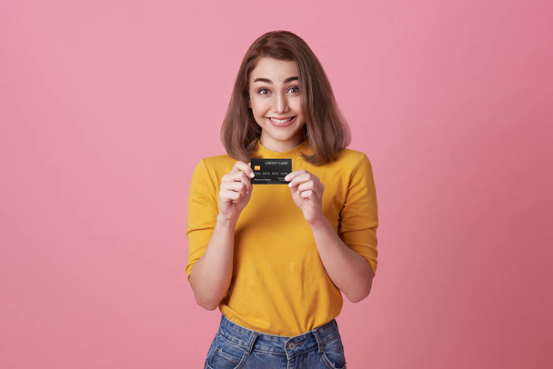 Χαρούμενη χαρούμενη γυναίκα που απολαμβάνει να δείχνει την πιστωτική της κάρτα απομονωμένη σε ροζ φόντο. - Φωτογραφία, εικόνα