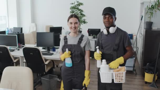 Medium lange slow motion portret van jonge Afro-Amerikaanse man en blanke vrouw werken in schoonmaakbedrijf staan in open kantoorruimte kijken naar camera - Video