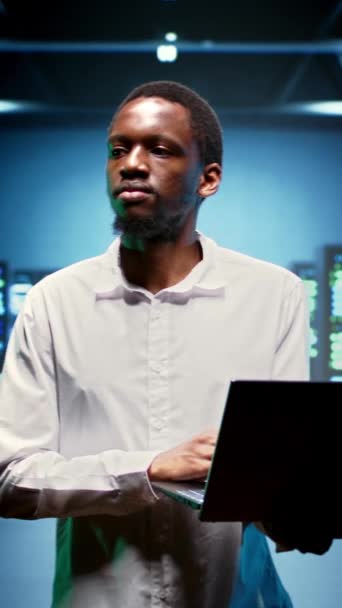 Вертикальне відео афроамериканського IT-фахівця, що йде між операційними мейнфреймами у високопродуктивній обчислювальній серверній кімнаті, забезпечуючи ідеальні умови роботи. Енергія обладнання експертного моніторингу - Кадри, відео