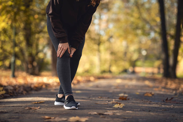 Low section of woman feeling knee injury during jogging in the park  - Photo, Image