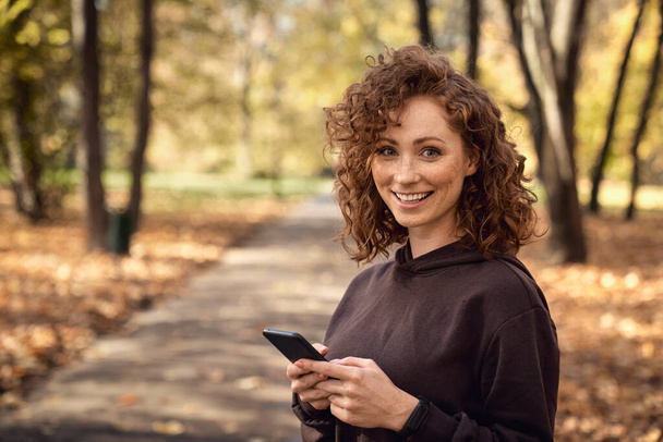 Portrait of caucasian woman browsing mobile phone with fun during the jogging activity  - Foto, Bild