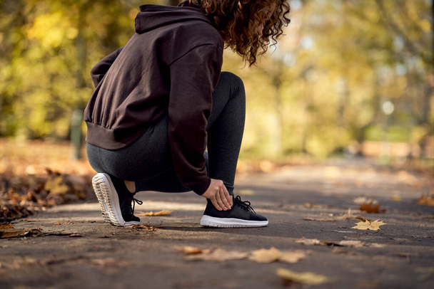 Side view of woman squatting and feeling ankle injury during jogging in the park - Valokuva, kuva