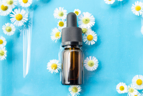 A bottle or bottle for essential oil with a pipette, lies in the water surrounded by flowers on a blue background. Background for advertising, beauty industry, cosmetology, medicine - Foto, Imagen
