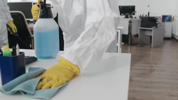 Średniej sekcji powolne ujęcie nierozpoznawalnego specjalisty noszącego na powierzchni biurka środki ochrony przeciwrozbryzgowej detergentu dezynfekującego i wycierającego go ściereczką z mikrowłókna - Materiał filmowy, wideo