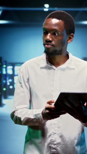 Vidéo verticale technicien afro-américain dans un établissement de haute technologie abritant des superordinateurs, des périphériques de stockage et des pièces de réseau fournissant de grandes quantités de ressources informatiques. Spécialiste faisant serveur - Séquence, vidéo