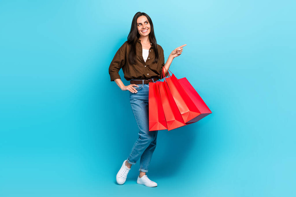 Full length photo of shopaholic fashionista young woman pointing finger empty space packages purchase isolated on blue color background. - Φωτογραφία, εικόνα