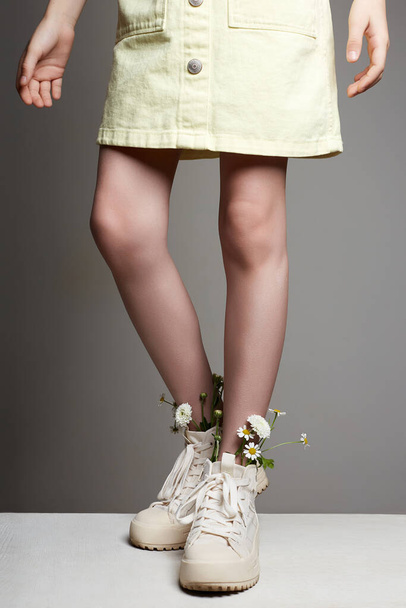 κοριτσίστικα πόδια σε λευκά παπούτσια με λουλούδια χαμομηλιού. Κοριτσάκι με κομψές μπότες - Φωτογραφία, εικόνα
