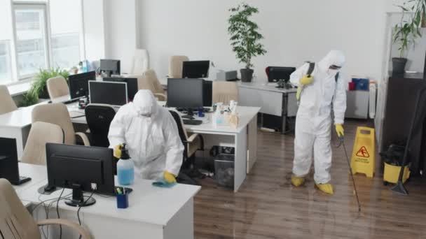 検疫中に近代的なオープンスペースのオフィスを消毒保護スーツを身に着けている2つの消毒サービスの専門家の高角度ショット - 映像、動画