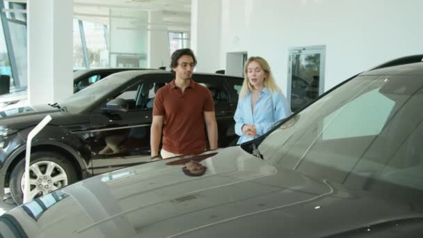 Różnorodne etnicznie młode małżeństwo wybiera crossover samochód do zakupu w nowoczesnym salonie dealerskim - Materiał filmowy, wideo