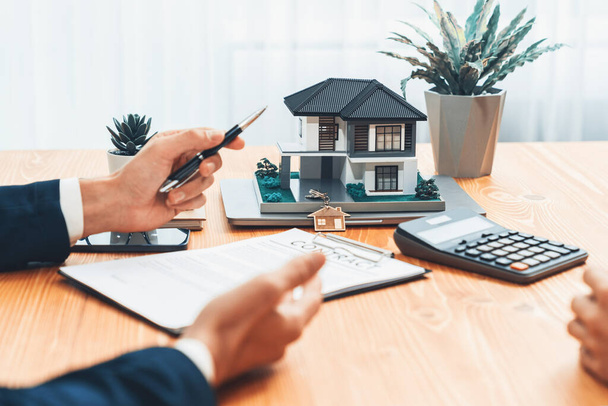 House model is displayed on wooden meeting table with in the blurred background of real estate agent and client discuss terms and conditions of house loan or rental lease contract. Entity - Photo, Image