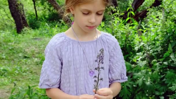 Ein trauriges Mädchen blickt auf eine von ihr gepflückte Blume mitten im Wald. Hochwertiges 4k Filmmaterial - Filmmaterial, Video