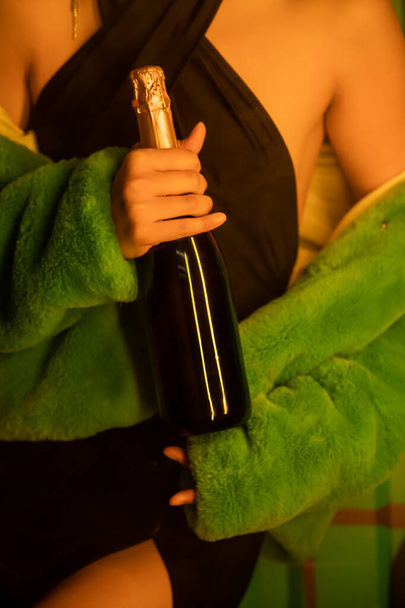 ナイトクラブで喫煙の近くにシャンパンを持っているドレスとジャケットのスタイリッシュな女性のクロップビュー - 写真・画像