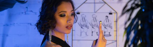 Модная азиатка в платье делает селфи на смартфоне в ночном клубе с неоновым светом, баннер - Фото, изображение