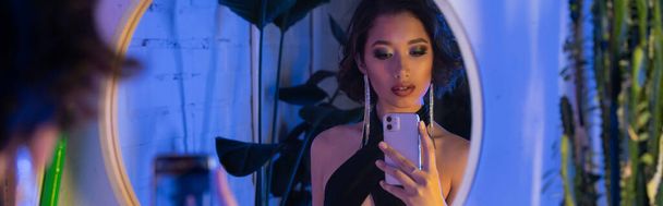 moda joven asiático mujer tomando selfie en smartphone cerca espejo y plantas en night club, banner - Foto, imagen