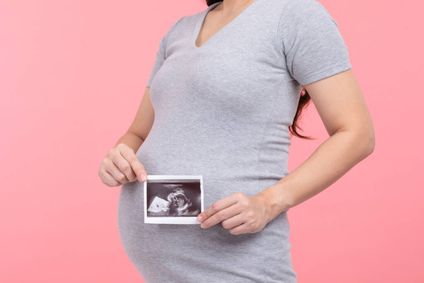 Happy Pregnant Woman standing smile holding ultrasound image stroking big belly with love isolated on pink background,Pregnancy of young woman enjoy with future life,Motherhood and Pregnant Concept - Foto, Imagen