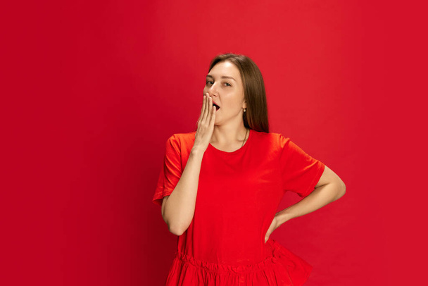 Retrato de una mujer joven cubriendo la boca con la mano, sintiendo sueño, bostezando sobre el fondo rojo del estudio. Me siento cansado. Concepto de emociones humanas, estilo de vida, juventud, moda, anuncio - Foto, Imagen