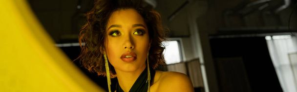 Sebevědomá a stylová asijská žena dívající se na zrcadlo ve žlutém světle v nočním klubu, prapor - Fotografie, Obrázek