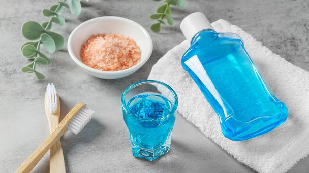 Mundspülung in Glas und Zahnbürste mit rosa Salz auf grauem Tisch, Zahnpflege - Foto, Bild