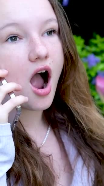 překvapení dospívající dívka mluvit na telefonu smích radovat se otevřená ústa wow stojí na ulici v květinách teenager tulipán jaro bílý telefon v rukou  - Záběry, video