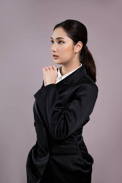 Confident young businesswoman stands on isolated background, posing in formal black suit. Office lady or manager with smart and professional appearance. Enthusiastic - Photo, Image