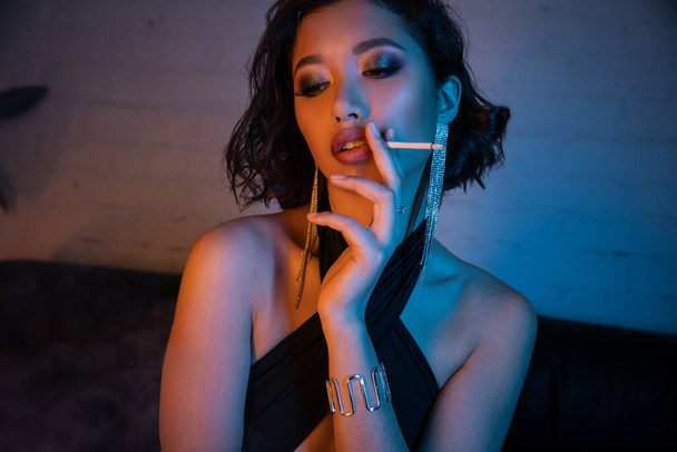 Confiante e sexy asiático mulher fumar cigarro enquanto passar tempo no clube noturno com luz de néon - Foto, Imagem