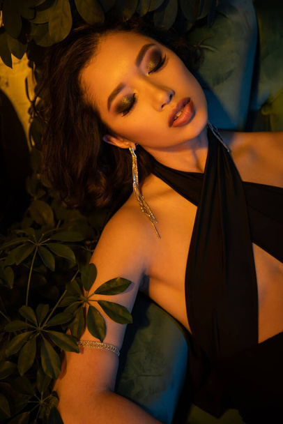 Trendy young asian woman in evening outfit sitting on armchair in night club with lighting - Foto, afbeelding