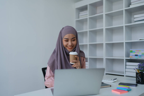 Portré egy muszlim nőről, aki laptopot használ és kávét iszik. - Fotó, kép
