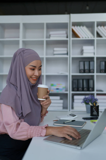 Porträt einer muslimischen Frau, die Laptop benutzt und Kaffee trinkt - Foto, Bild