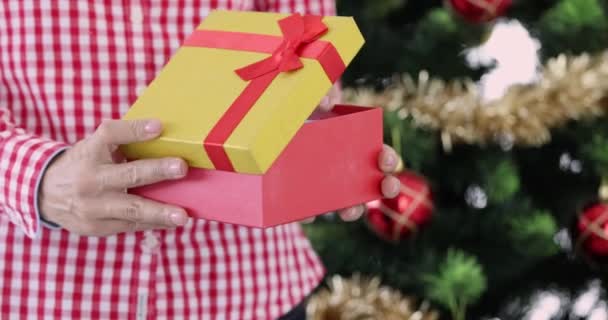 Mujer de pie cerca del árbol de Navidad con el regalo de Año Nuevo rojo en sus manos película 4k. concepto de regalos de Navidad - Metraje, vídeo